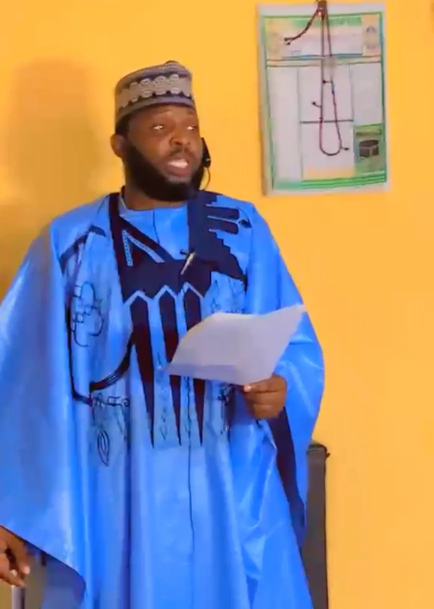 A graduate in a flowing blue robe addressing his students.