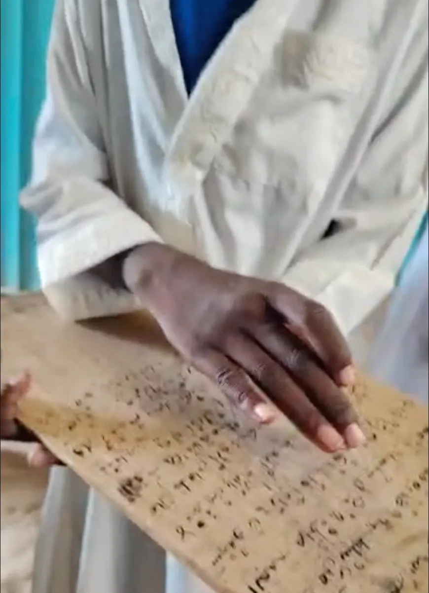 A student's hand resting on a traditional wooden tablet inscribed with Qur'anic verses.